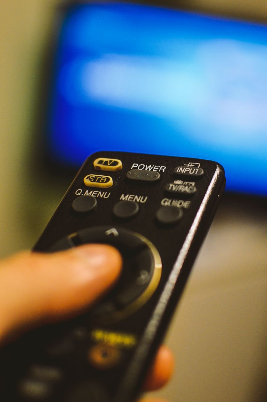 Hand holding smart TV remote control in modern home entertainment setting